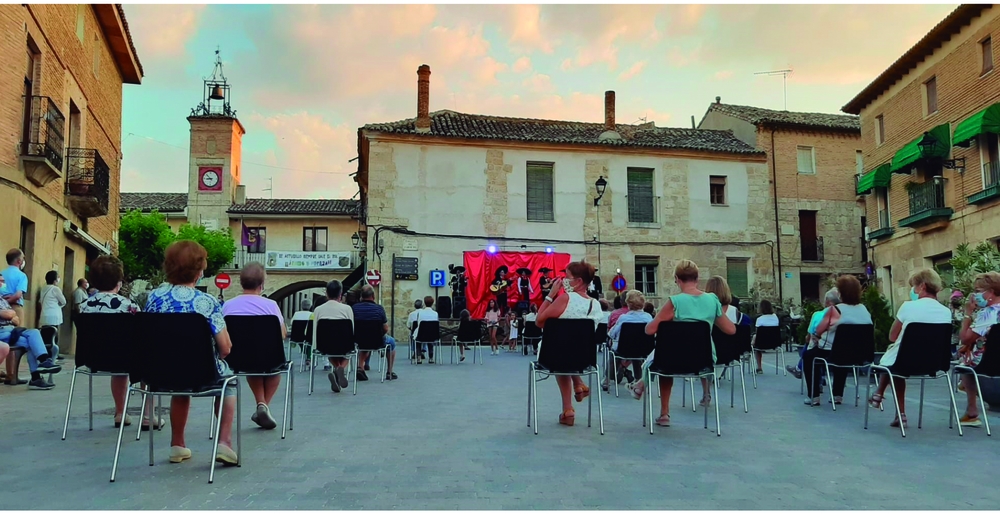 En la imagen vemos cómo se colocaron las sillas en una de las actuaciones del Verano Cultural, atendiendo a la separación social por familias. Y, por supuesto, todos con mascarillas. Al fondo, el Ayuntamiento y las chimeneas redondas propias de Astud  / ASTUDILLO